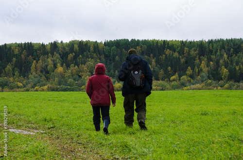 Two travelers are walking along a green field and a dirt road. Family travel © Yakovlev