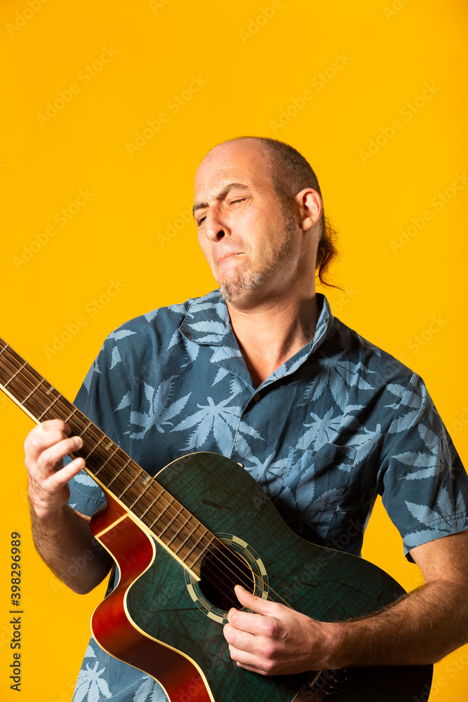 Obraz premium Portrait of a Musician while plying his blue acoustic guitar against a yellow background