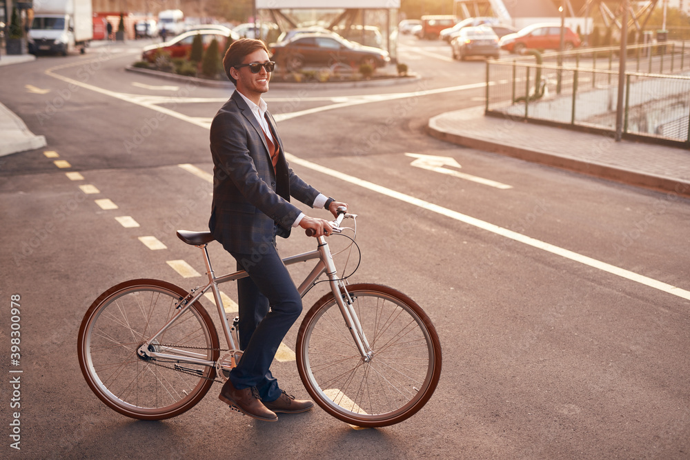 Cheerful trendy businessman with bicycle on street