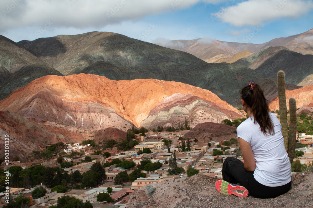 Woman sitting on the mountain, looking at the town of Purmamarca.
