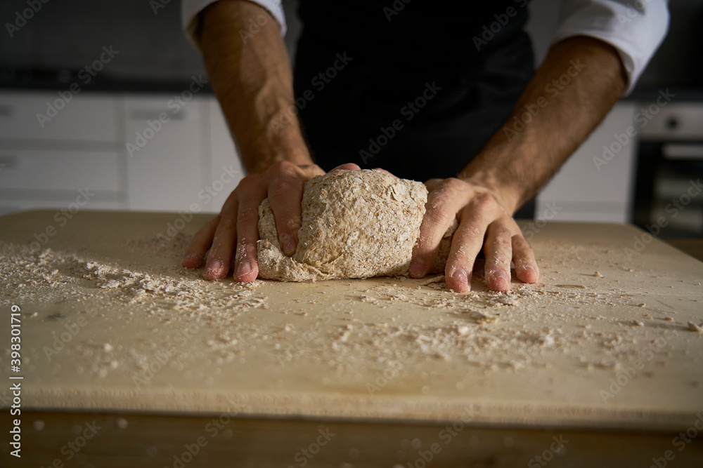 The hands of the strong man knead the dough from which they will make bread, pasta, cake or pizza. In his kitchen he carries on the tradition of homemade pasta. A cloud of white flour flies like dust. The hands of the strong man knead the dough from which they will make bread, pasta, cake or pizza. In his kitchen he carries on the tradition of homemade pasta. A cloud of white flour flies like dust.