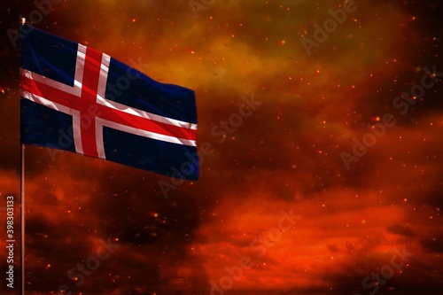 Fluttering Iceland flag mockup with blank space for your text on crimson red sky with smoke pillars background. Troubles concept.