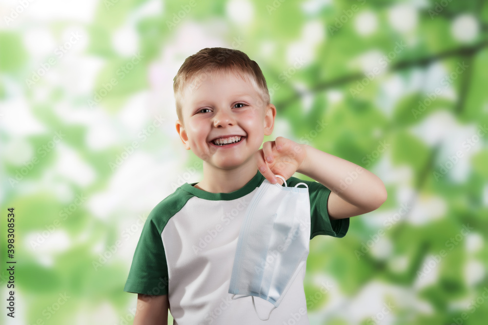 Happy little boy smiling and holding face mask in hand on green Happy little boy smiling and holding face mask in hand on green