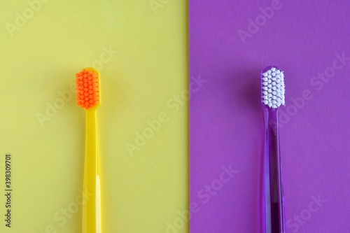 two plastic purple and yellow toothbrushes on color block paper background. Health care concept. Man and woman teeth hygiene. Living together.