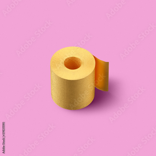 Roll of golden color painted toilet paper on a pink background with soft shadows