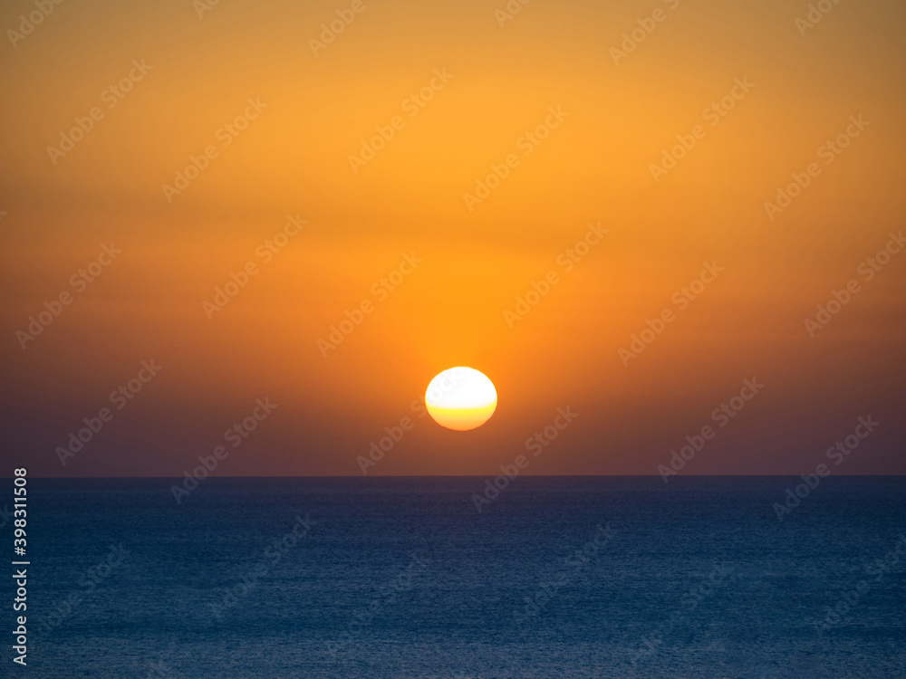 Orange sun in the sunset sky over the blue sea