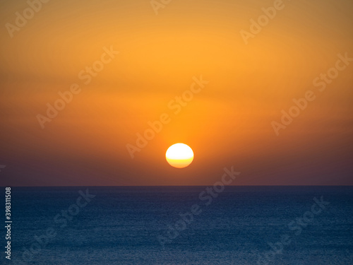 Orange sun in the sunset sky over the blue sea