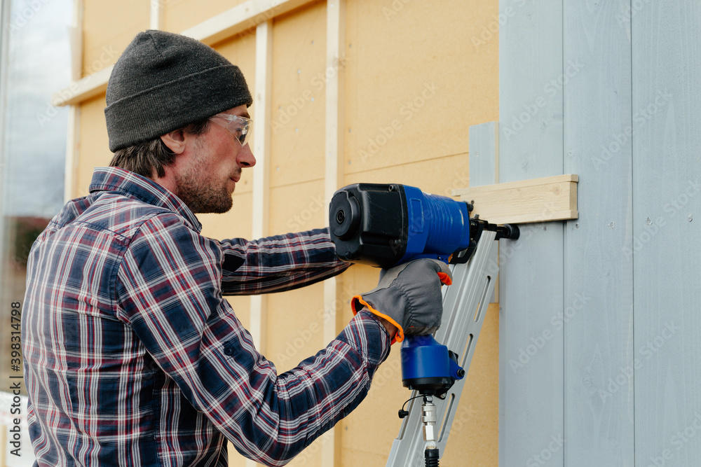 Man with nail gun installing siding on house Man with nail gun installing siding on house