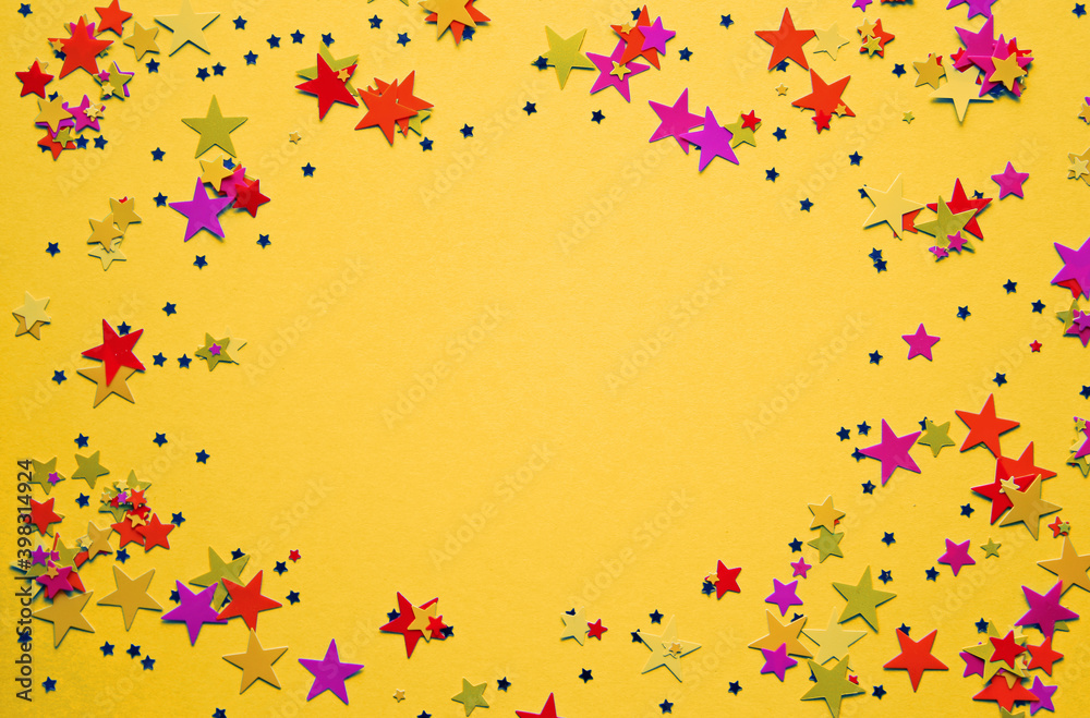 Multicolored stars confetti on yellow background. Festive confetti. Copy space. Top view. Space for text.