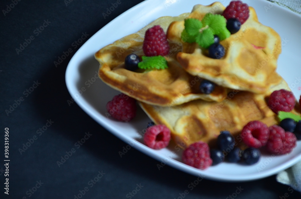 Homemade Belgium Waffles with fresh blueberries for breakfast. White plate, Viennese waffles with raspberries and mint. quick delicious breakfast on black background. top view copy space