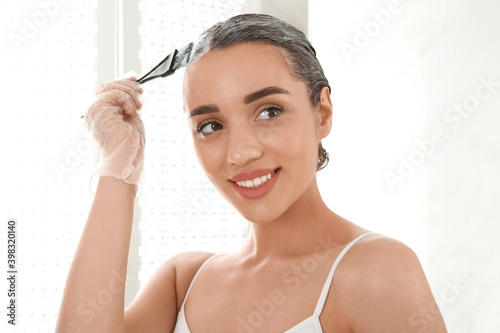 Young woman applying dye on hairs indoors