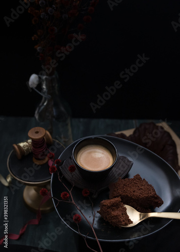 Closeup view of an elegant tray with a foamy coffee, a slice of cake and a golden spoon over it with a little piece of cake.