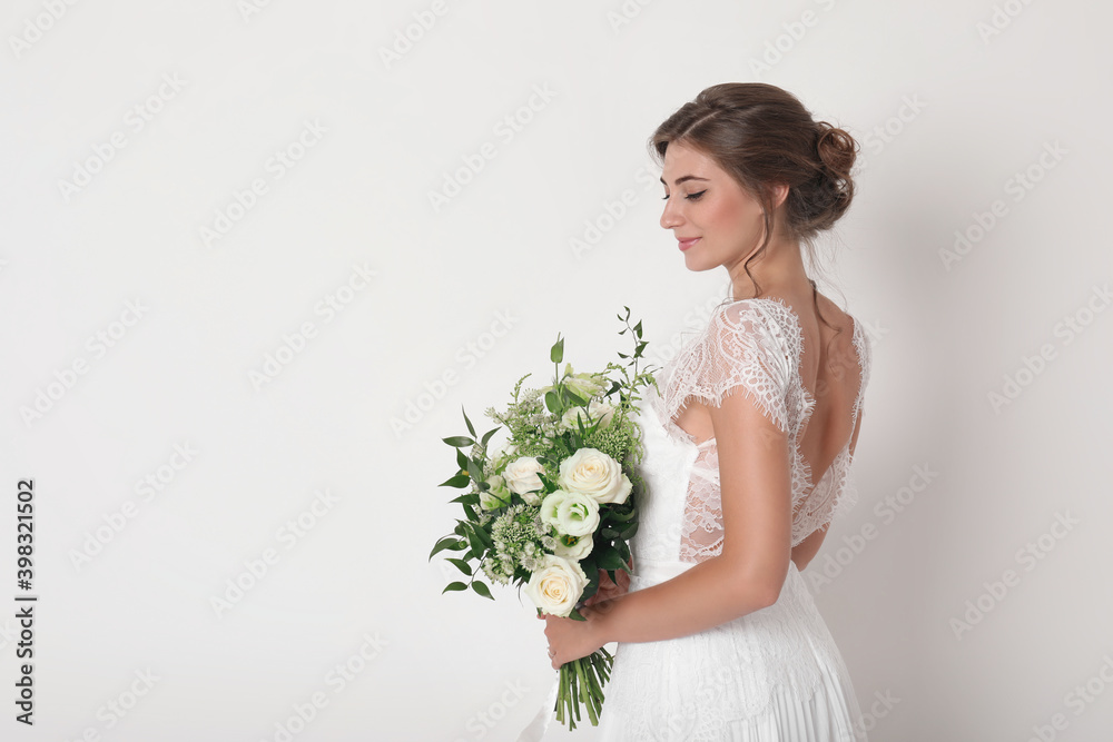 Young bride wearing wedding dress with beautiful bouquet on light background. Space for text Young bride wearing wedding dress with beautiful bouquet on light background. Space for text