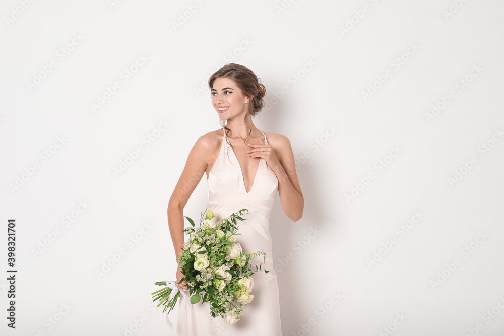 Young bride wearing wedding dress with beautiful bouquet on light background Young bride wearing wedding dress with beautiful bouquet on light background