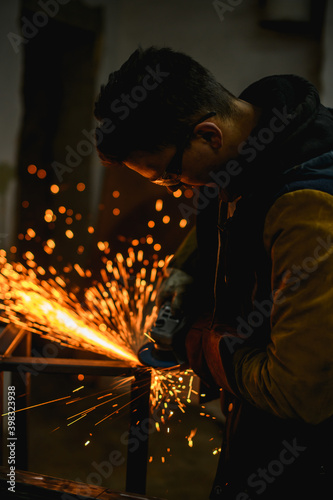 Selective focus of locksmith sharpening metallic profile with bright sparks in unlit workshop 