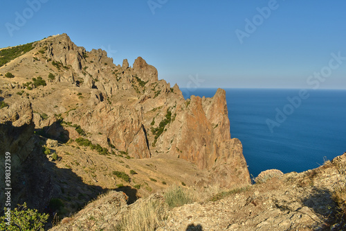 Beautiful landscape with rocks, green bushes on their slopes, sea and clear blue sky 