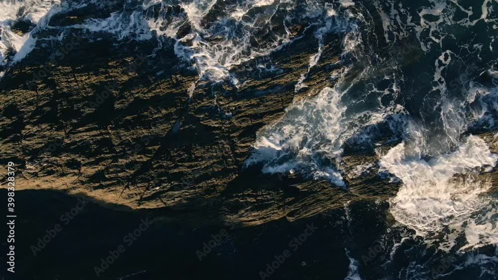 Vuelo sobre preciosas olas chocando contra rocas al atardecer