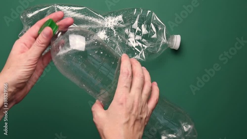 Female hands fold and crush transparent PET plastic bottle for recycling. Closeup crumpled water bottels on green background. Reuse reduce recycle household trash. Go green and zero waste concept photo