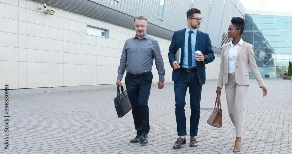 Mixed-races business partners walking the street in city and talking about work. Multi ethnic men and women speaking while strolling outdoor. African American businesswoman and Caucasian businessmen.