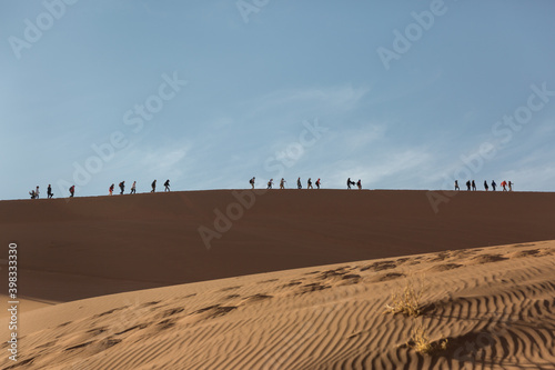 A group of tourists walks along the top of the dune against the background of the blue sky. Namibia