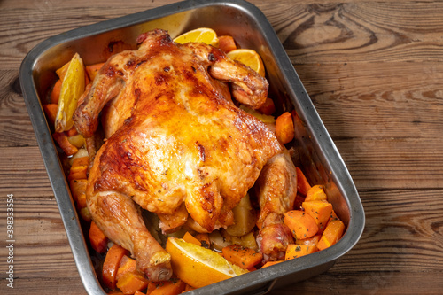 Whole baked chicken with carrots and oranges on a wooden table. Close-up and top view