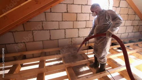 Worker with a hose is spraying ecowool insulation in the attic of a house. Insulation of the attic or floor in the house photo