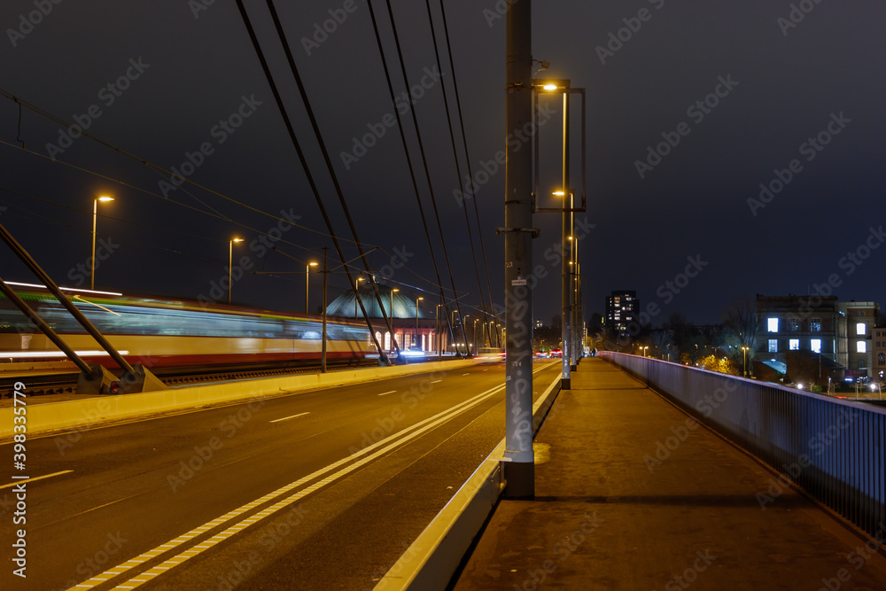 Night scenery of public transportation trams or train  with motion blur and pedestrian pathway on suspension bridge without vehicle and traffic in Düsseldorf, Germany.