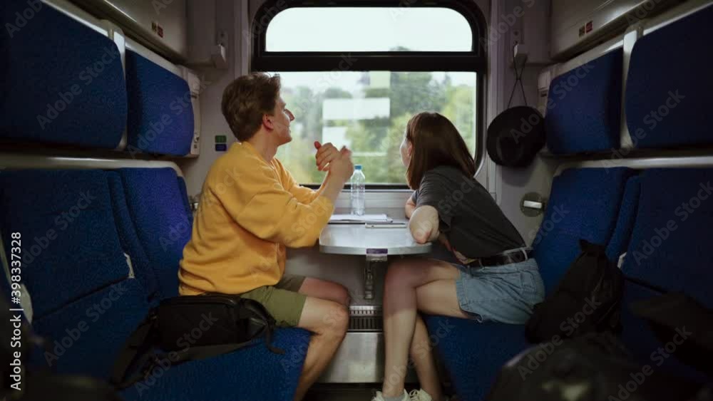 Beautiful young couple sitting in a train at a table on the road and communicates with a smile on his face. A couple in love travelsby train. Beautiful young couple sitting in a train at a table on the road and communicates with a smile on his face. A couple in love travelsby train.