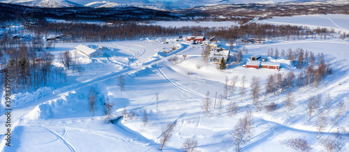 Scenic aerial view on small Tarna Vilt village in Swedish Lapland in winter cover, frosty sunny day. Roads, houses, frozen lakes, birch trees with Scandinavian mountains at background photo