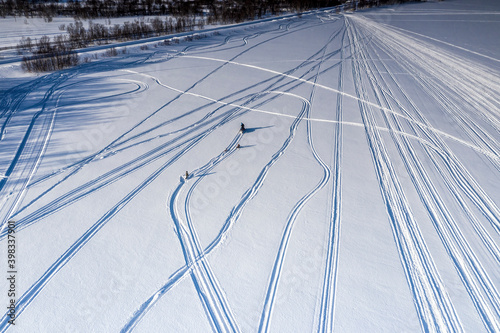 Scenic aerial view on adult driver pulled two children on snow racers with snowmobile, one child fall into snow - lost pulling rope. Holiday activity, white frozen mountain lake Joesjo Swedish Lapland