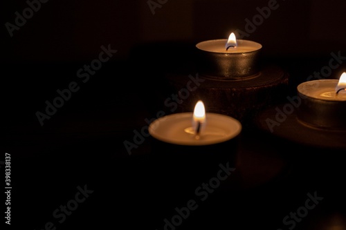 selective focus of three small candles lit in the dark with flashes of light with religious meaning