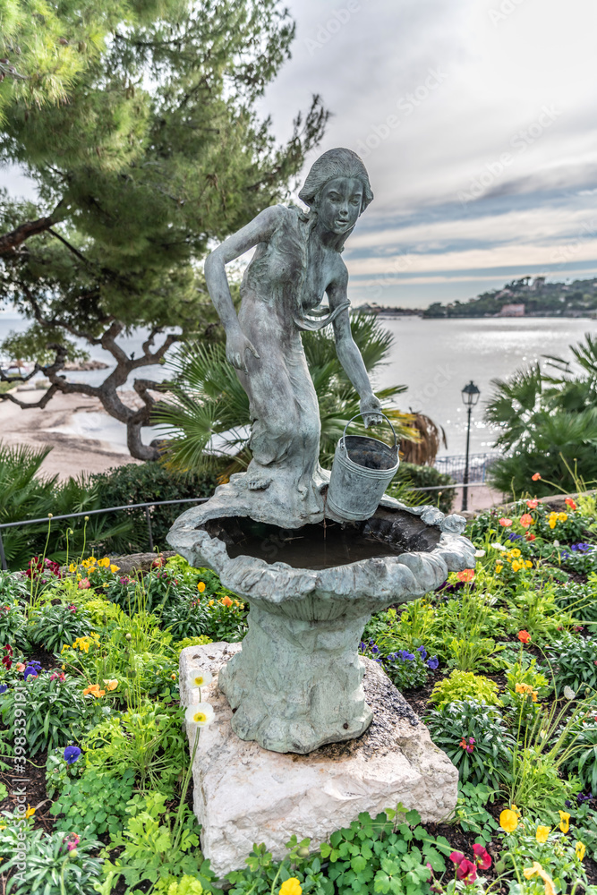 Obraz premium Porteuse d'eau dans un massif de fleurs en pierre en bord de mer 