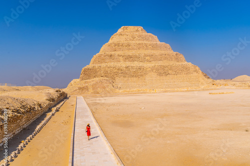 A young girl in a red dress walking in the Stepped Pyramid of Djoser, Saqqara. Egypt. The most important necropolis in Memphis. The first pyramid in the world photo