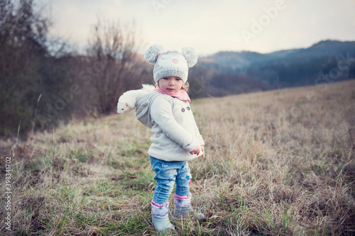 A little girl is outside with her pet. Cute baby girl wearing a ferret in a hood. The child and his living furry pet. Autumn in the countryside. Friendship of children and animals. Walking with a