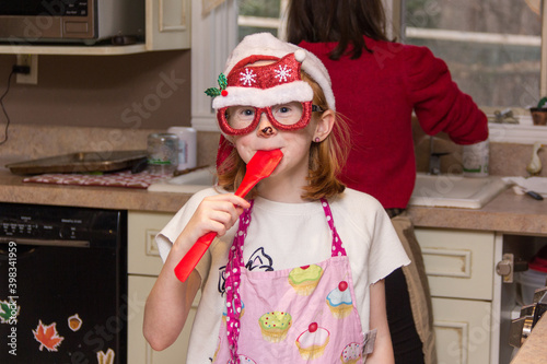 Young girl sucking on a red stirring batter spoon while making holiday cookies photo