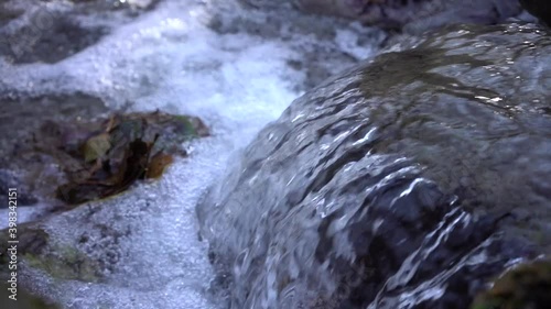Mountain stream with crystal clear drinking water flows down the stones. Autumn leaves falling into the spring
