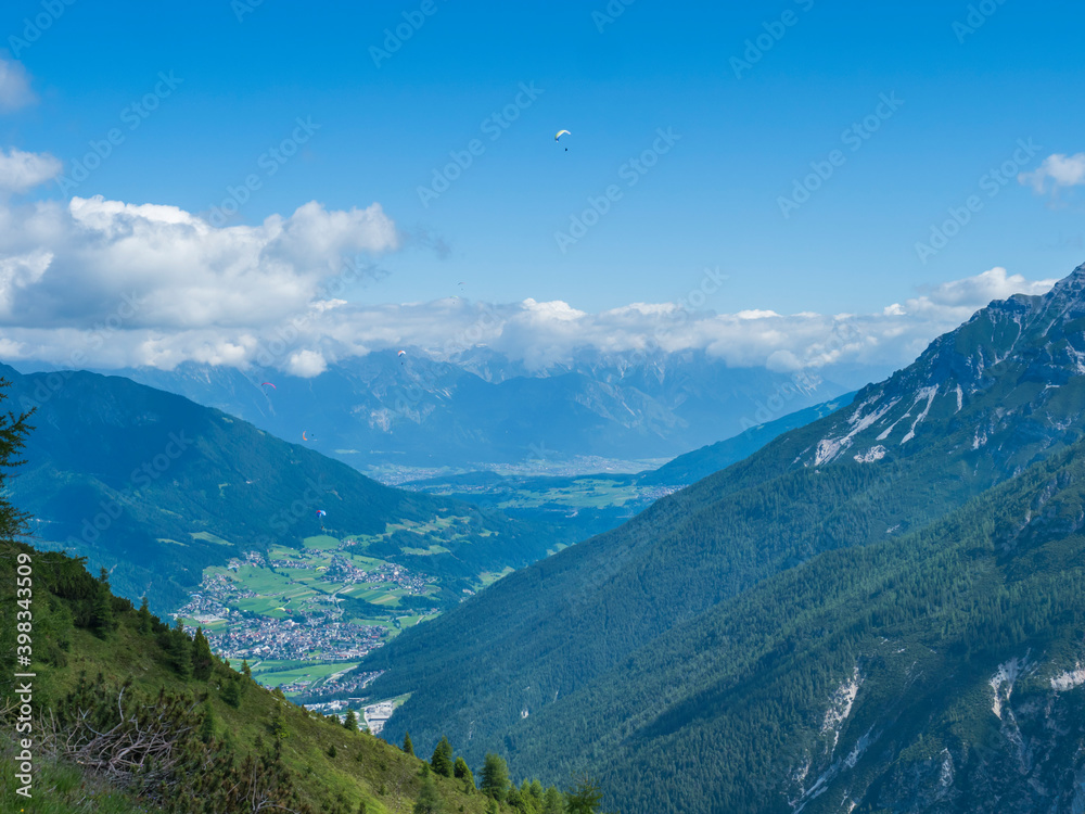 View over green Stubai valley and Neustift im Stubaital village from Elferhutte with moutain peaks and kites. Tirol Alps, Austria, Summer blue sky, white clouds
