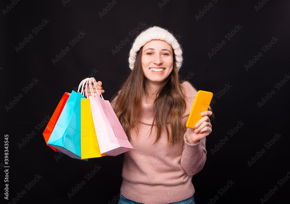 An excited young woman about her online shopping. She is holding some colourful bags and her phone. over black background. An excited young woman about her online shopping. She is holding some colourful bags and her phone. over black background.