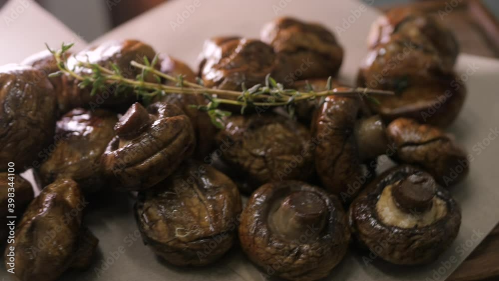 Grilled mushrooms with herbs lie on white craft paper. Hot, appetizing dish rotates and the camera flies around. Grilled mushrooms with herbs lie on white craft paper. Hot, appetizing dish rotates and the camera flies around.