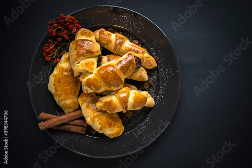 Freshly baked sweet homemade rolls with jam sprinkled with powdered sugar and cinnamon, served on a plate on a dark background.