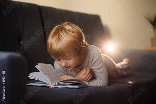 Child little boy reading a book while lying on the sofa