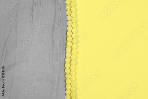 Texture of gray cotton fabric of ultimate color tone and shiny and tender necklace on illuminating and bright yellow background as a trend of the year 2021. Trendy beautiful backdrop with copy space.