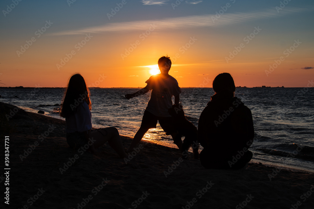 silhouette of a boy and some family members in the beautiful sunset. Enjoying the peaceful scenery while playing with his dog