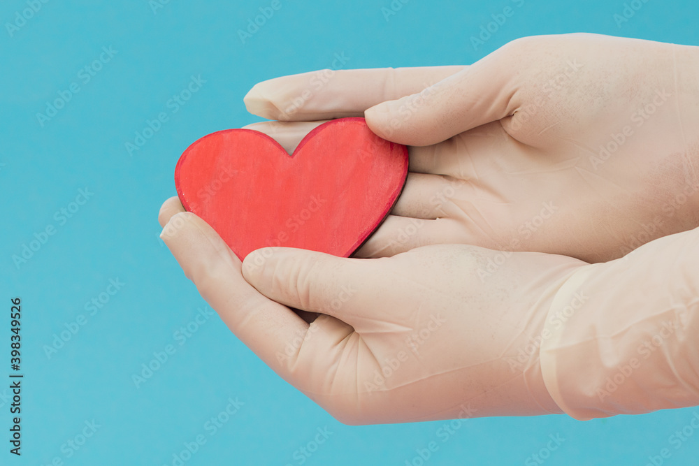 Hands in medical gloves hold a small red heart on a blue background. Protection from covid-19. Stay safe. Gratitude to doctors. Valentine's day.Horizontal photo, side View, close-up.