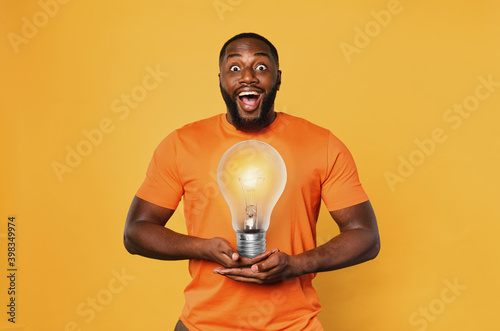 Fotografie Happy afro man holds a lightbulb with hands