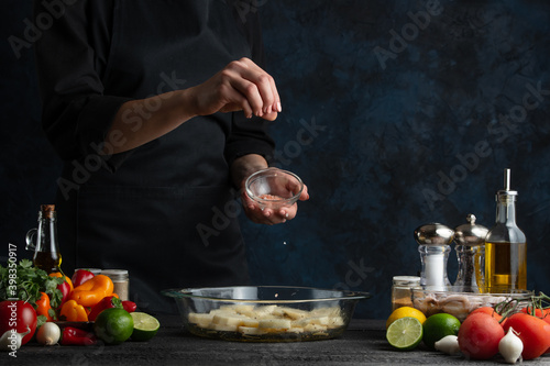 Fototapeta Naklejka Na Ścianę i Meble -  The professional chef squeezes lime juice on raw potatoes. Backstage of cooking traditional asian dish with seafood. Preparing delicious meal on dark blue background. Concept of cooking process.