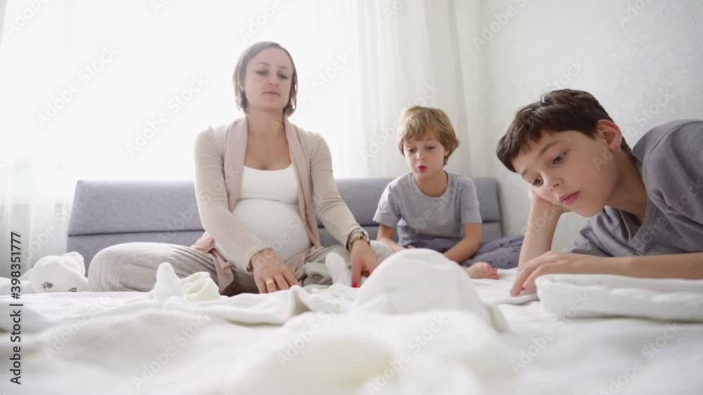 Pregnant woman sits on the bed with two sons and prepares things for the birth of a child. High quality 4k footage Pregnant woman sits on the bed with two sons and prepares things for the birth of a child. High quality 4k footage