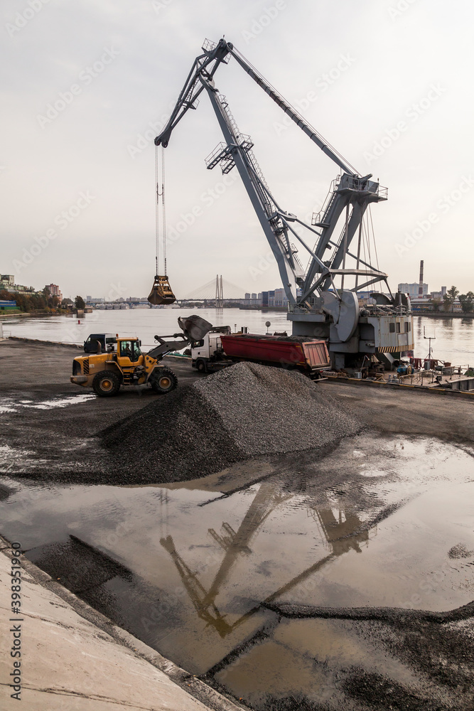 Yellow tractor with a bucket loading gravel into a truck at the port