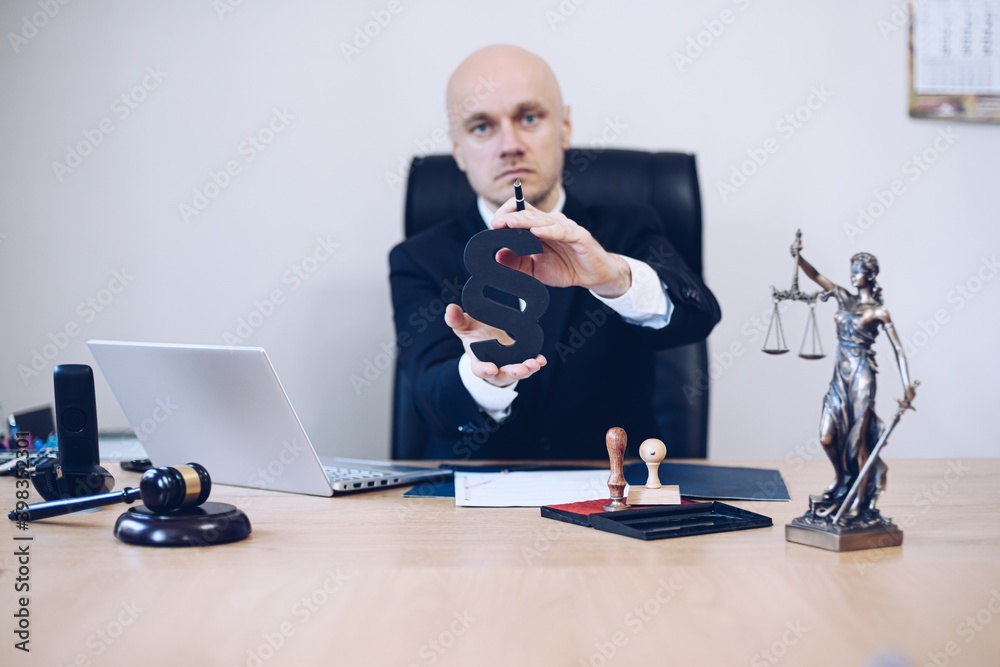Attorney in the office holds a paragraph in his hand as a sign of justice and law.