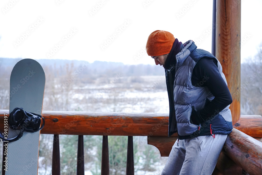 A guy in an orange hat in winter holds a cup of tea in his hands during a winter vacation in the mountains.
